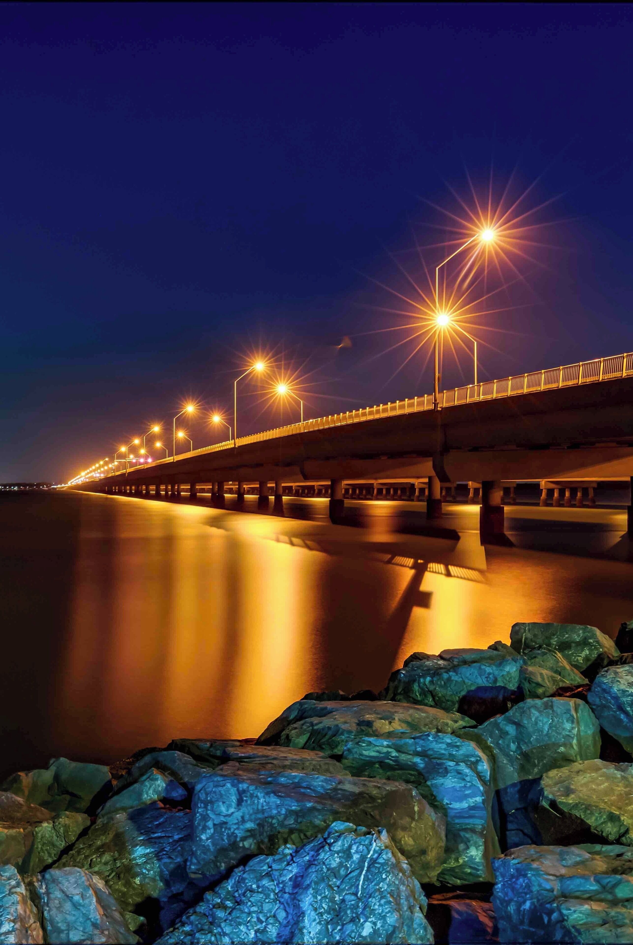 A nighttime view of a bridge with streetlights and a calm river below.