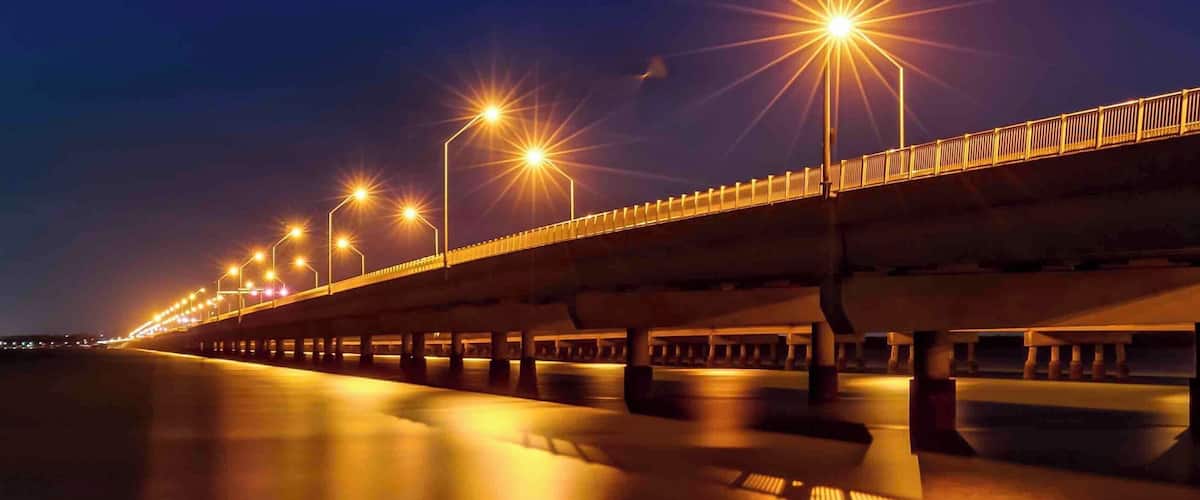 A nighttime view of a bridge with streetlights and a calm river below.