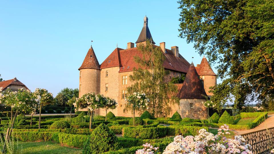 A historic castle with multiple towers, surrounded by well-manicured gardens and blooming flowers.