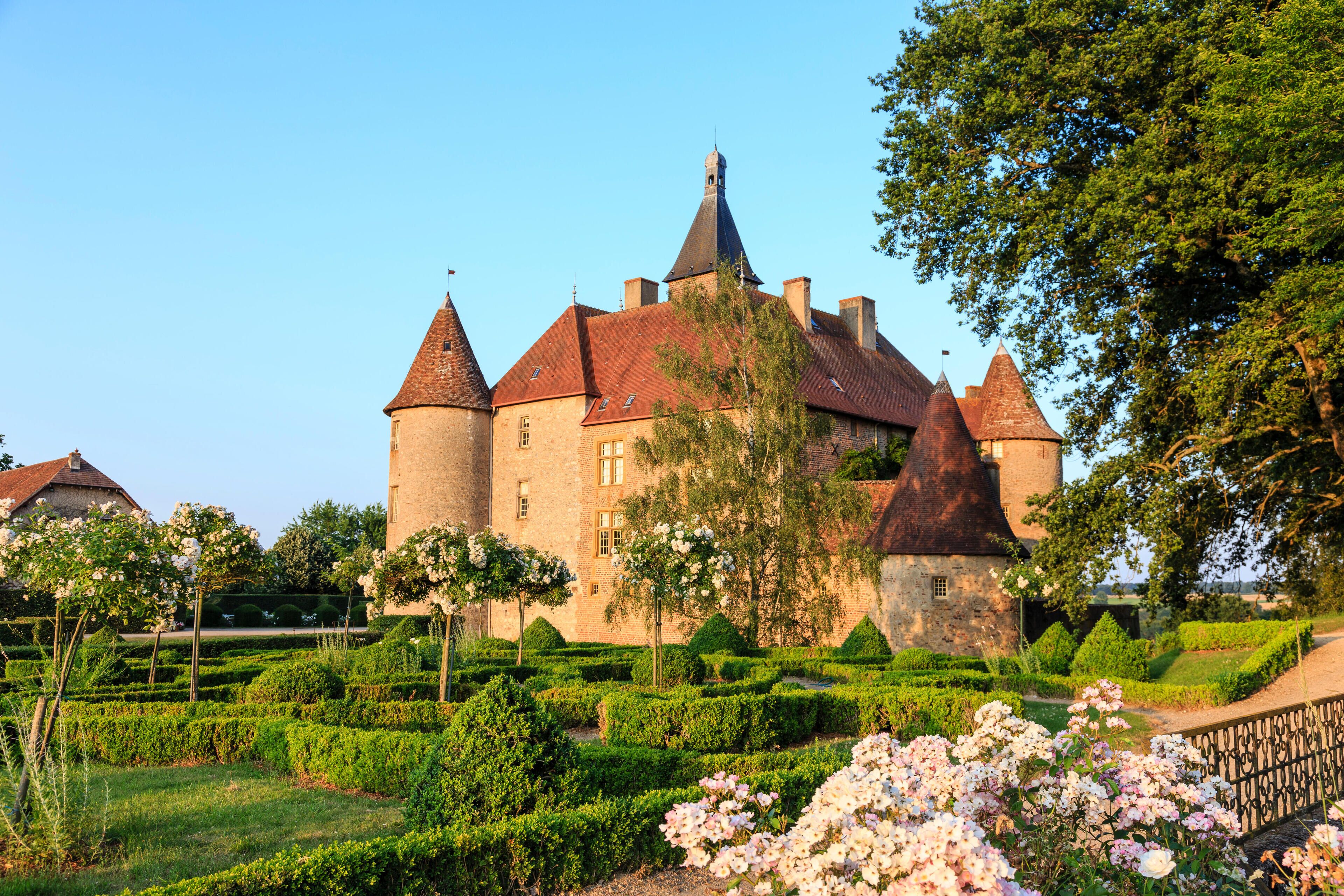 A historic castle with multiple towers, surrounded by well-manicured gardens and blooming flowers.