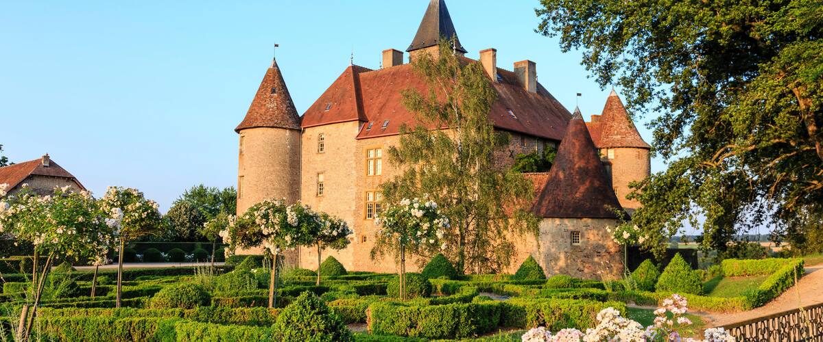A historic castle with multiple towers, surrounded by well-manicured gardens and blooming flowers.