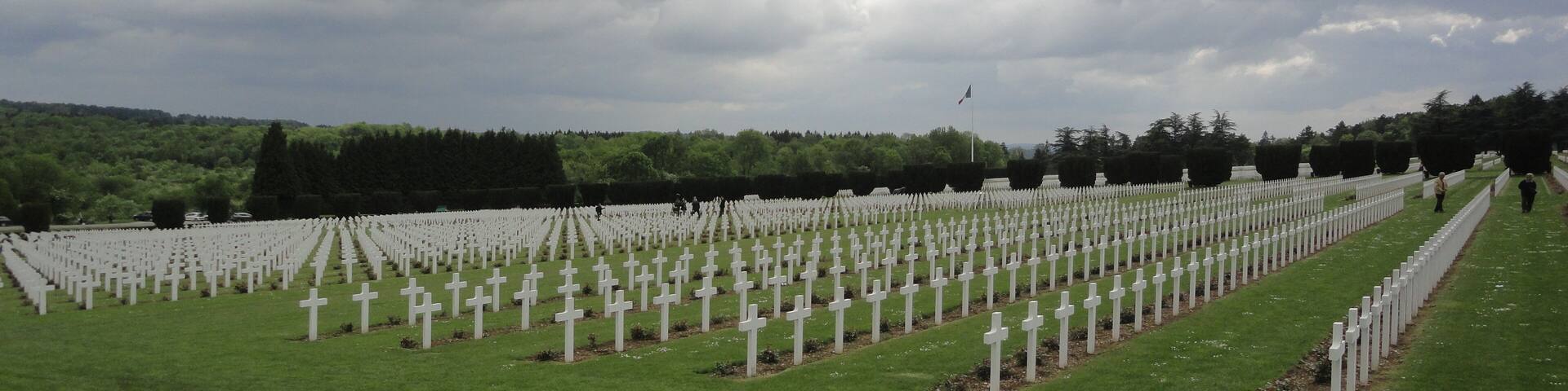 A cemetery with rows of white crosses under a cloudy sky.