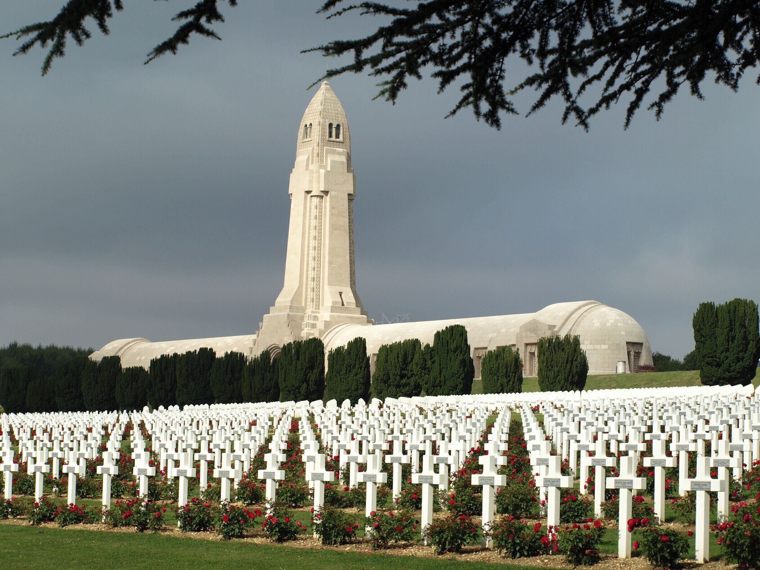 A cemetery with numerous white crosses and a large building with a tall tower in the background.