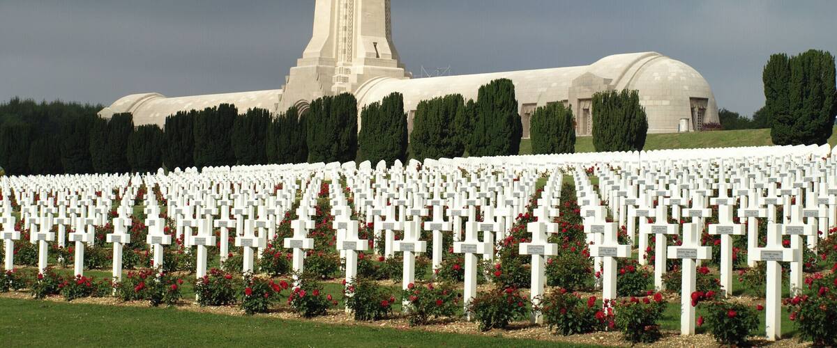 A cemetery with numerous white crosses and a large building with a tall tower in the background.