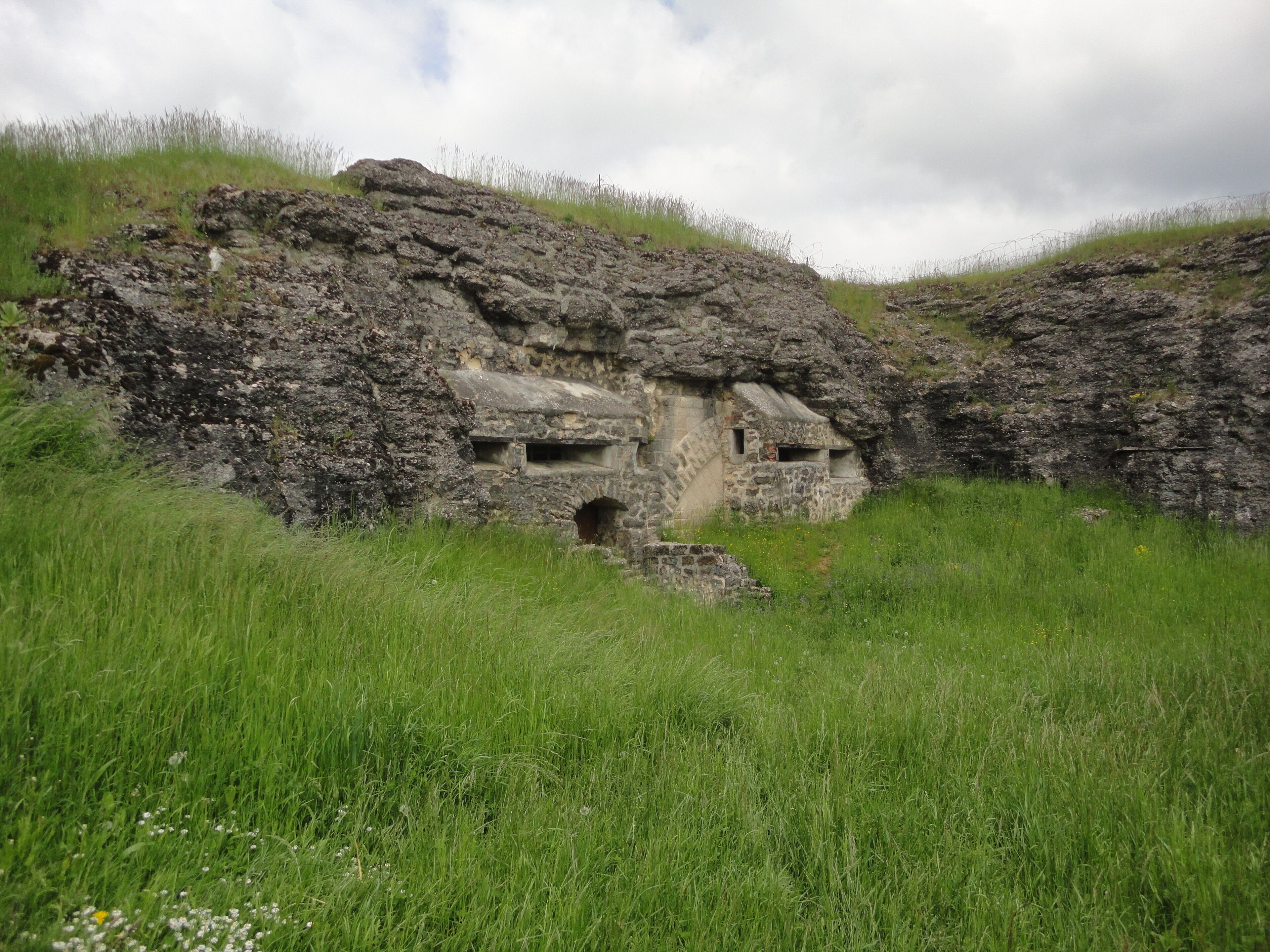 A stone structure with a cave-like entrance surrounded by grass and hills.