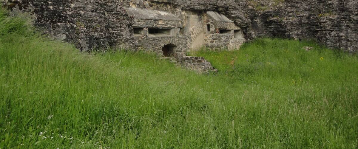 A stone structure with a cave-like entrance surrounded by grass and hills.