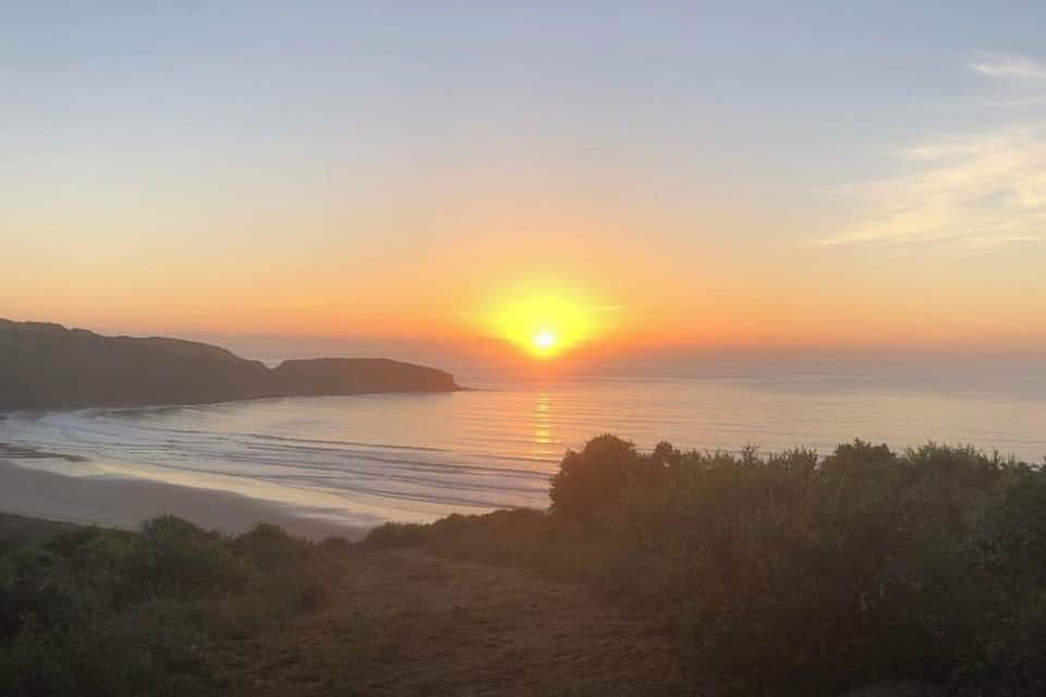 Un atardecer sobre un mar tranquilo con una masa de tierra a lo lejos.