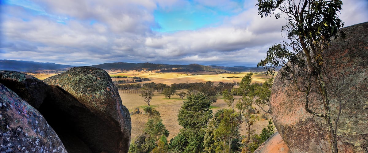 A landscape with large rocks, trees, and a distant view of hills and valleys.
