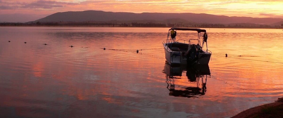 A boat anchored on calm water with a sunset in the background.
