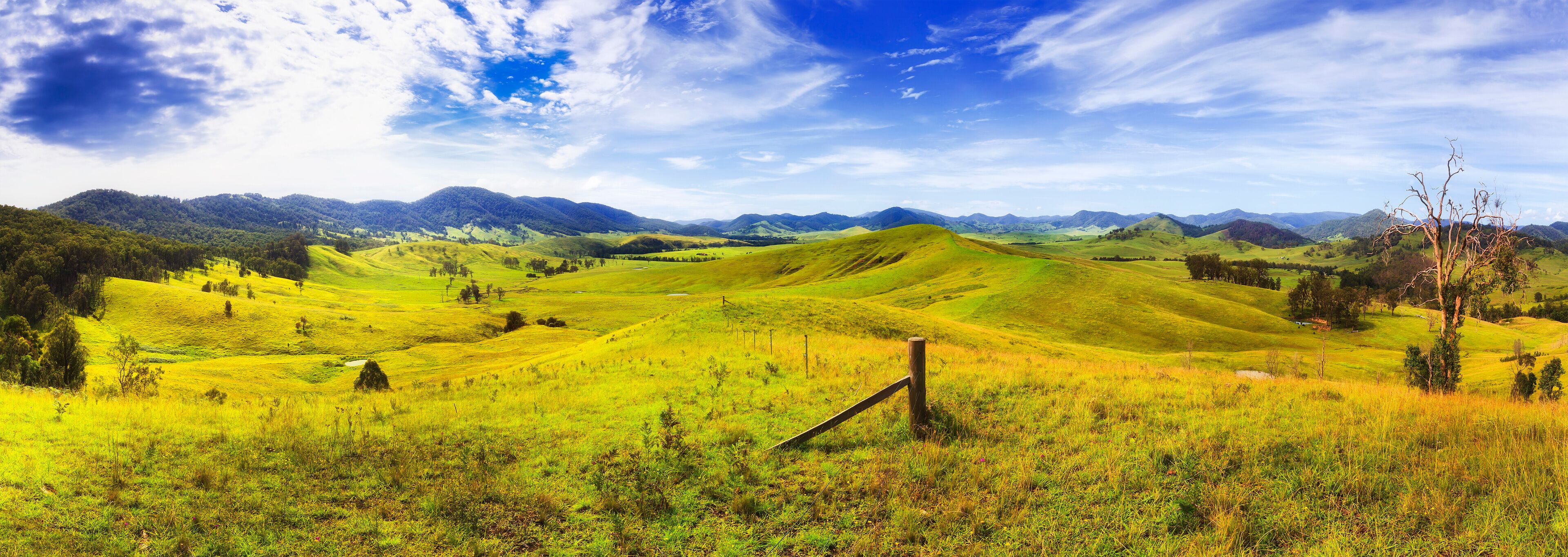 Rolling green hills, a wooden fence, and distant mountains under a partly cloudy sky.