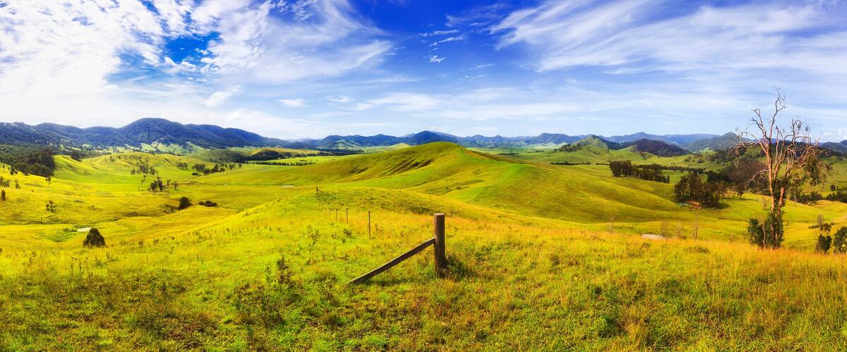 Rolling green hills, a wooden fence, and distant mountains under a partly cloudy sky.