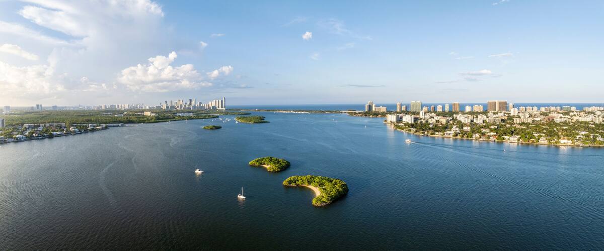 A coastal cityscape with a large body of water, several islands, and a dense urban area with high-rise buildings.