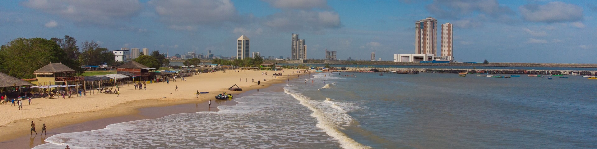 Aerial view of the sun-kissed beach meeting the foamy waves, with the iconic Eko Atlantic City buildings standing tall in the distance, Lagos, Lagos, Nigeria.