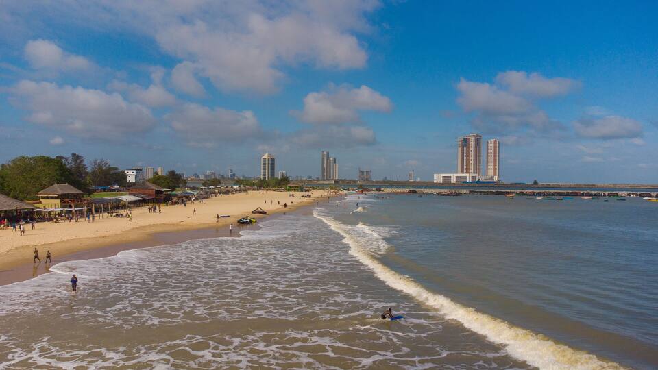 Aerial view of the sun-kissed beach meeting the foamy waves, with the iconic Eko Atlantic City buildings standing tall in the distance, Lagos, Lagos, Nigeria.