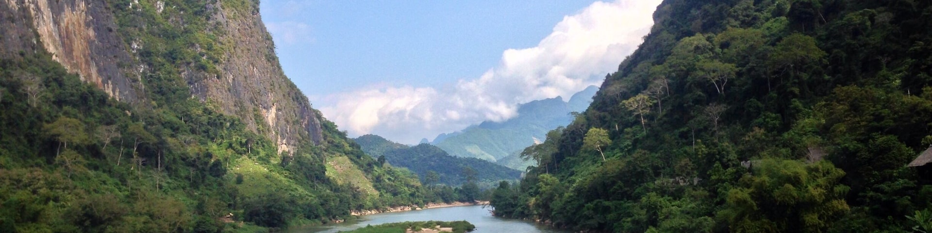 Un río flanqueado por montañas boscosas y empinadas bajo un cielo parcialmente nublado.