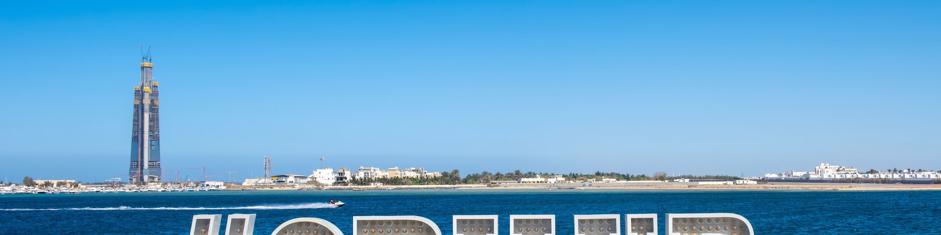 Une promenade en bord de mer avec une grande enseigne lumineuse qui affiche le mot-clé « #OBHUR » et, en arrière-plan, un grand immeuble.