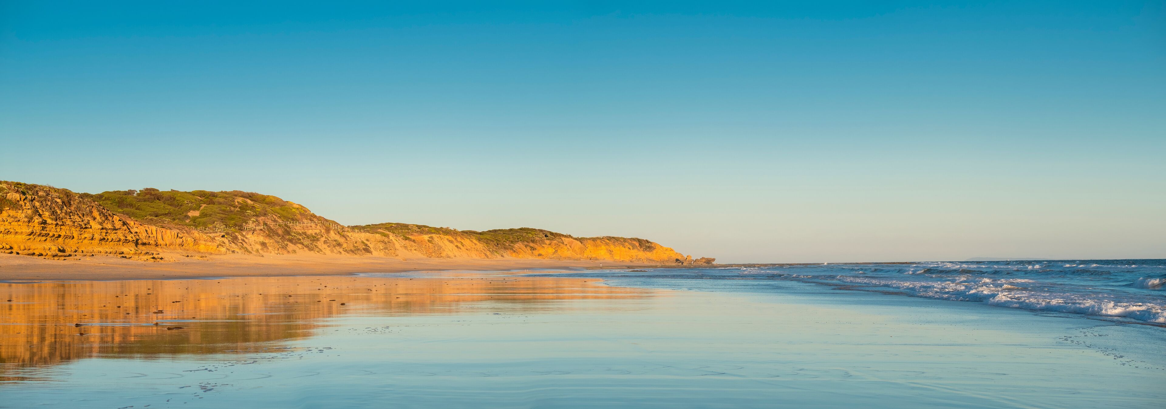A beach with a sandy shore, gentle waves, and a rocky cliff with sparse vegetation.