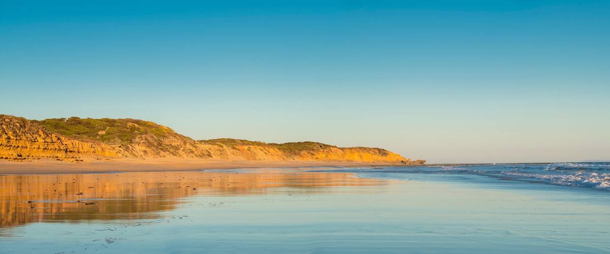 A beach with a sandy shore, gentle waves, and a rocky cliff with sparse vegetation.
