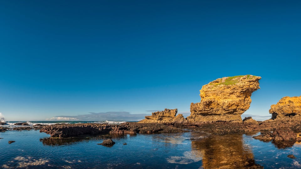 A coastal landscape with rocky formations and calm waters reflecting the sky.