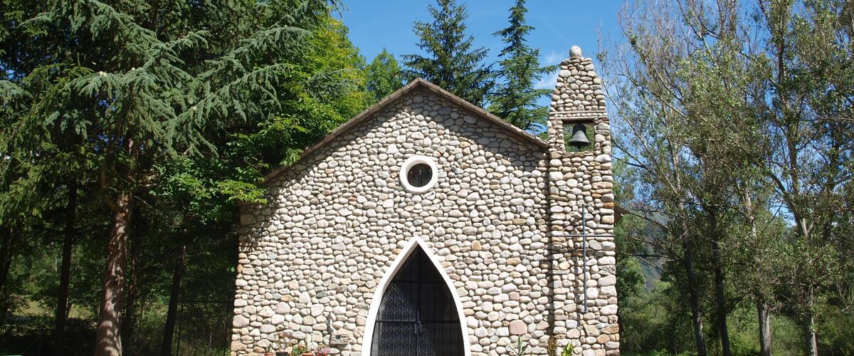 A stone church with a bell tower, surrounded by trees.