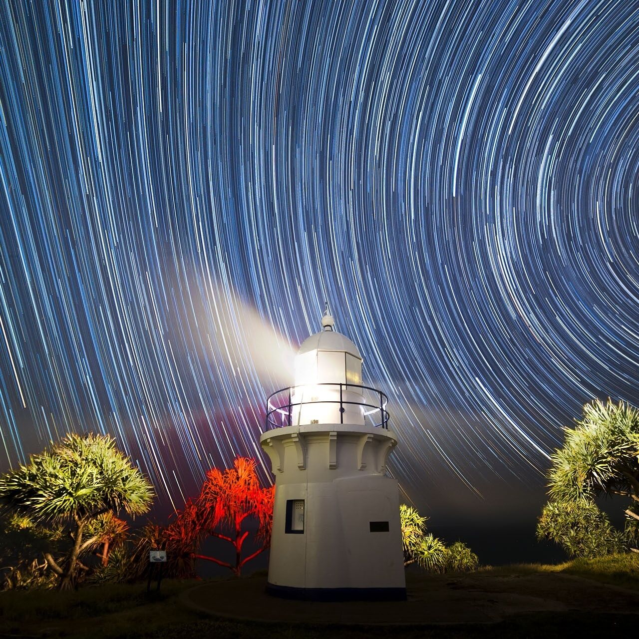 A lighthouse with star trails in the night sky.