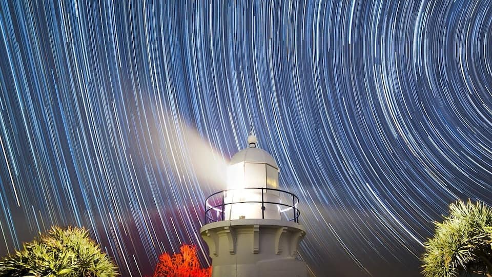 Um farol com rastros de estrelas no céu noturno.