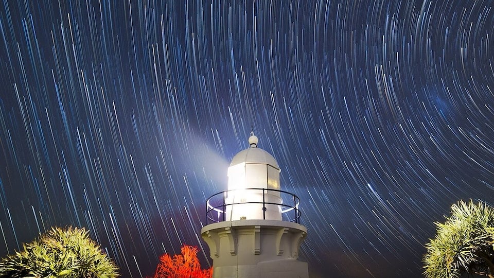 Um farol com rastros de estrelas no céu noturno.