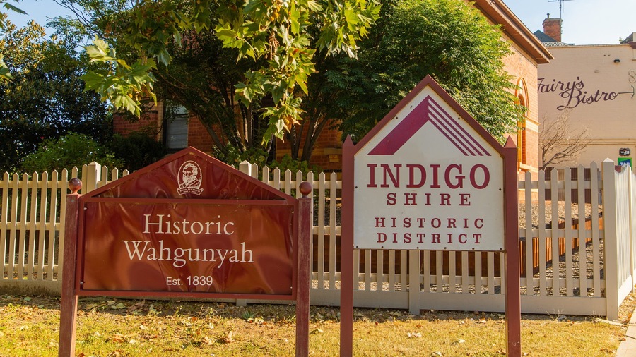 Letrero de distrito histórico para Indigo Shire, letrero de distrito histórico para Wahgunyah y una cerca de piquetes blancos.