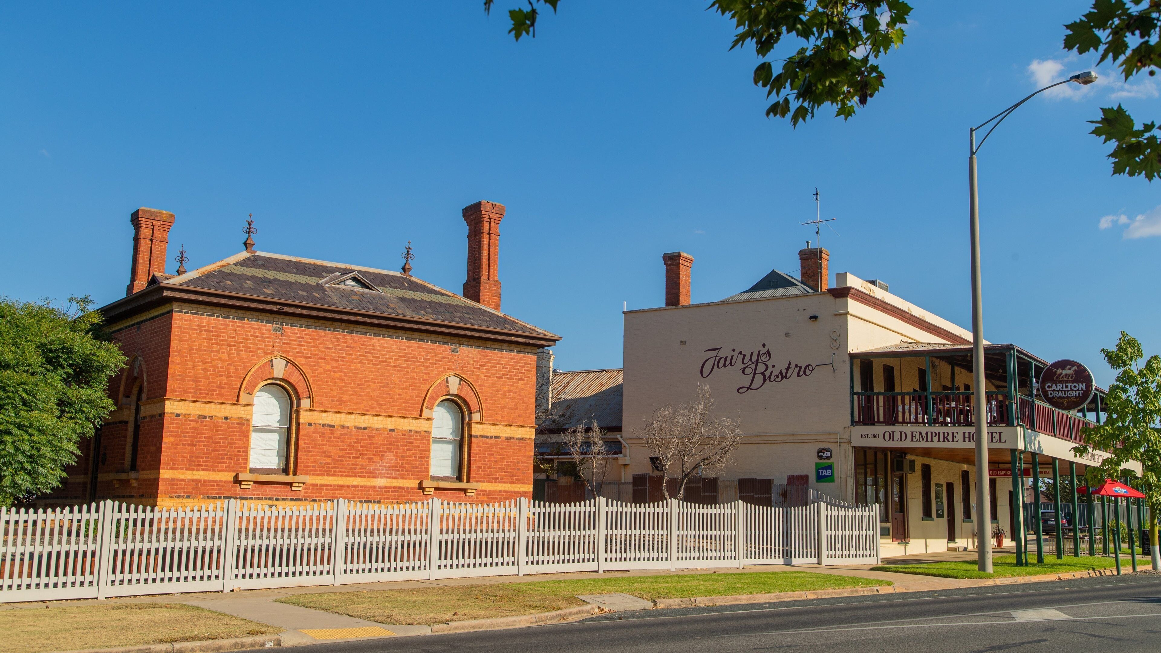 A red brick building with arched windows and a white picket fence.