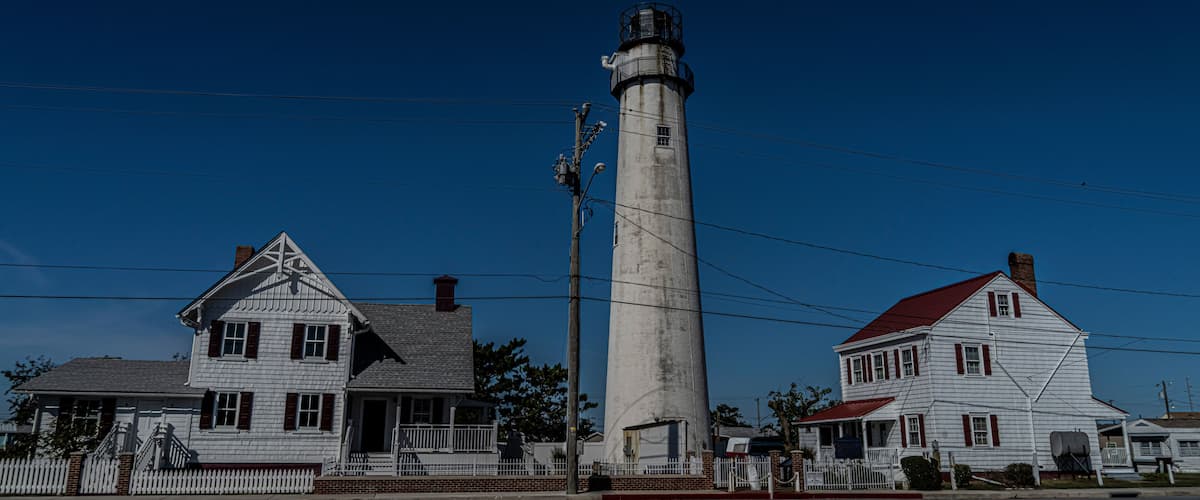 A lighthouse, two white houses with red roofs, and a white picket fence.