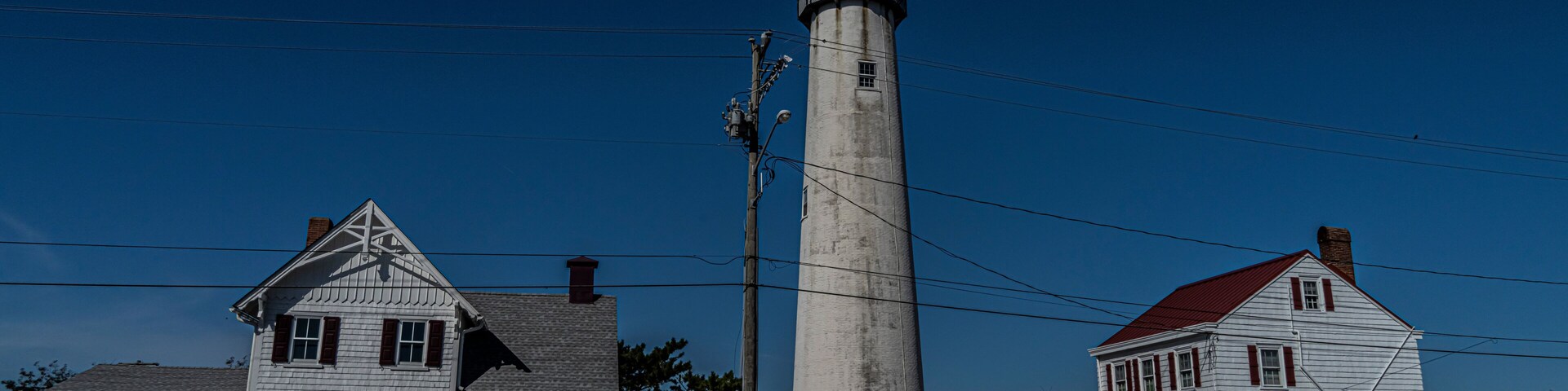 A lighthouse, two white houses with red roofs, and a white picket fence.