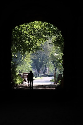 A cyclist rides through a dark tunnel into a bright, sunlit forest - Biking through a tunnel on the Katy Trail by the Missouri River