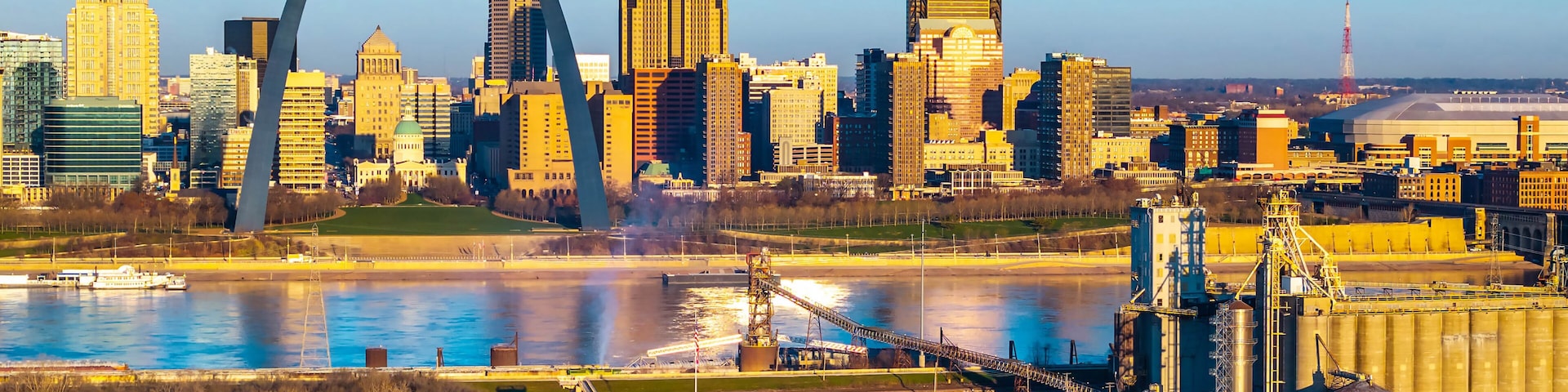 Un horizonte urbano con un puente arqueado destacado, un río y edificios industriales.