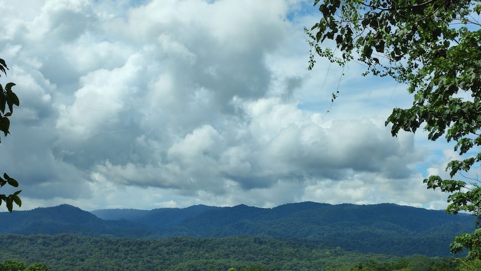 A mountainous landscape with dense green forests and a cloudy sky.