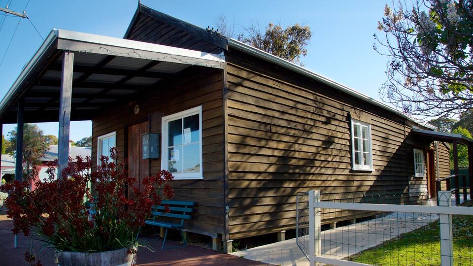A wooden house with a porch, a bench, and a fenced area.