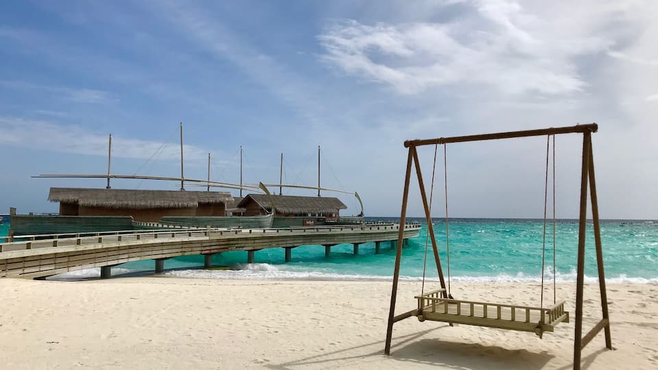 A beach with a swing set and a pier with overwater bungalows.