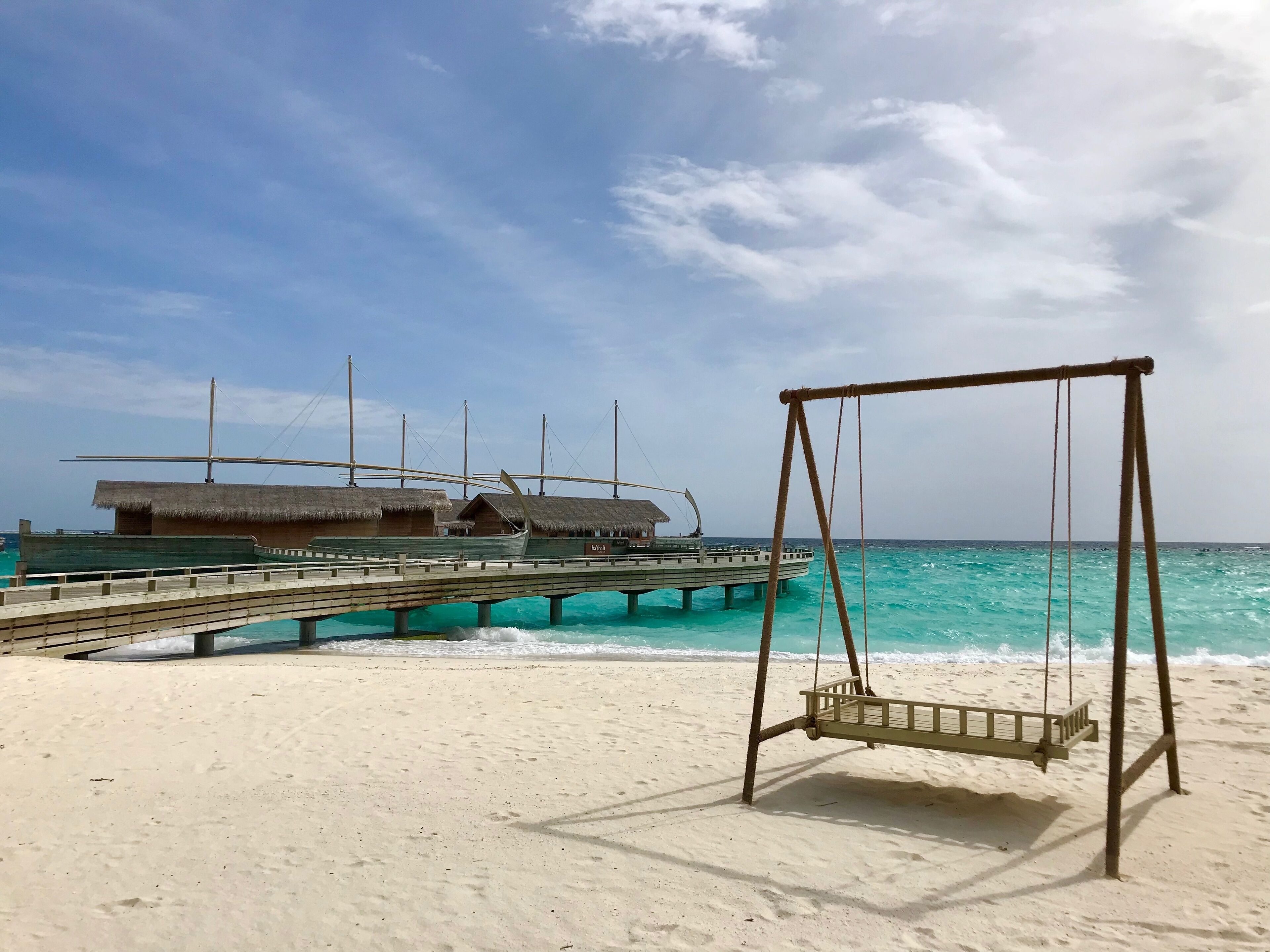 A beach with a swing set and a pier with overwater bungalows.