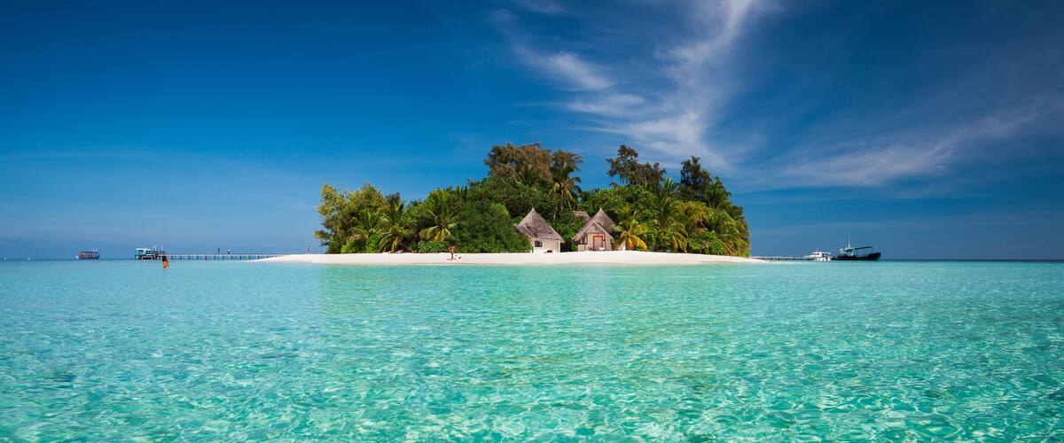 A tropical island with clear turquoise waters, a pier, and thatched-roof huts.