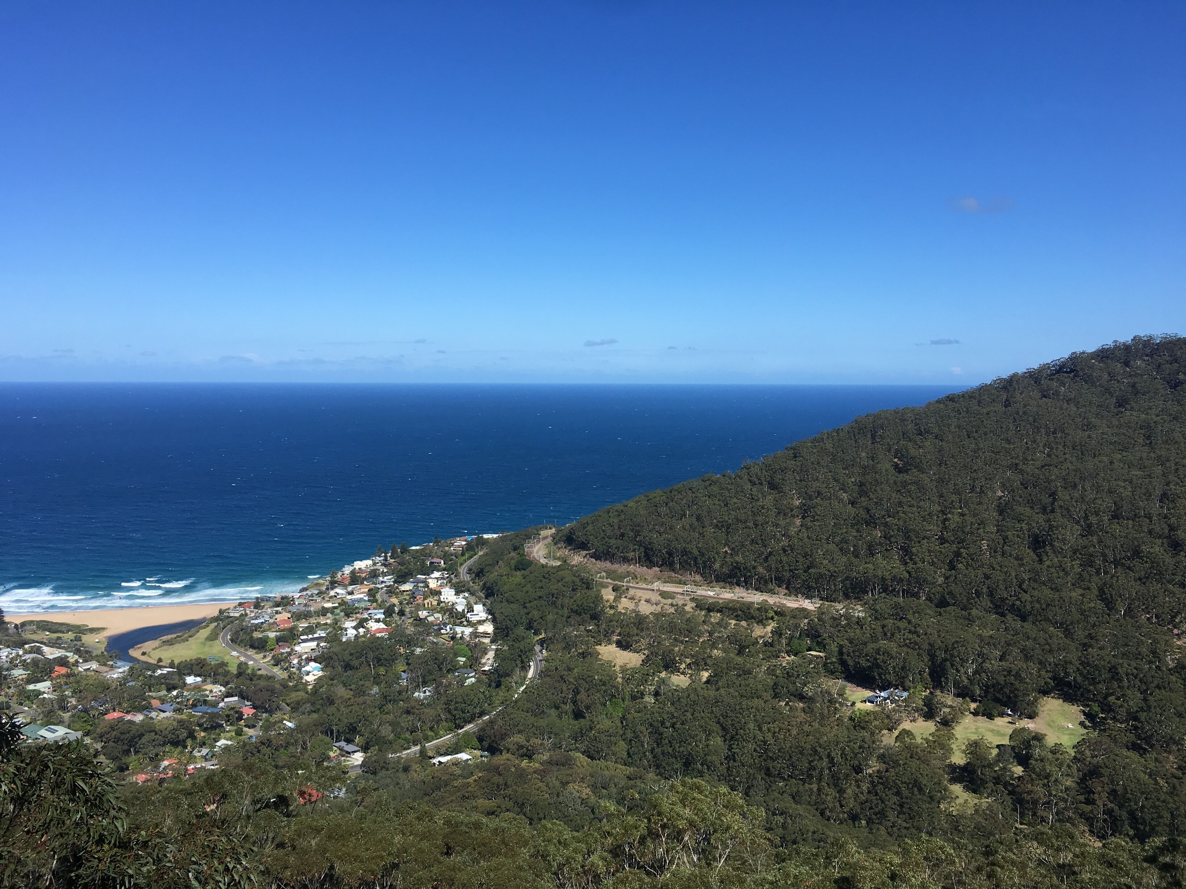 A coastal town nestled between forested hills, with a beach and ocean in the background.