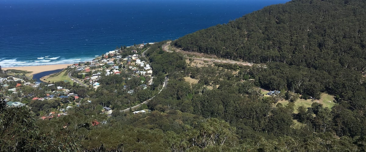 A coastal town nestled between forested hills, with a beach and ocean in the background.