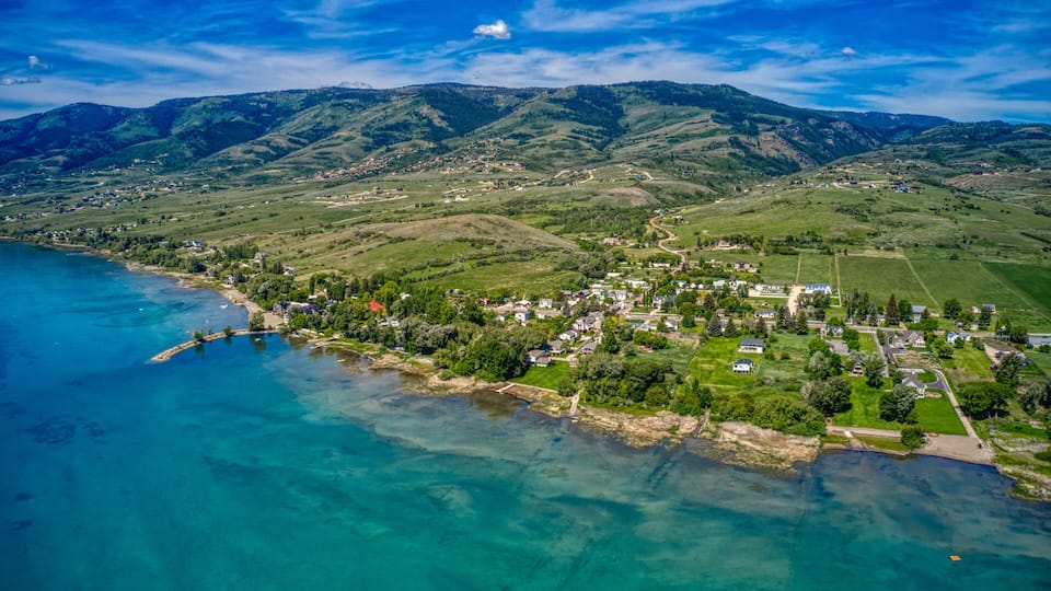 A coastal town with a clear blue sea, green hills, and a mountainous backdrop.