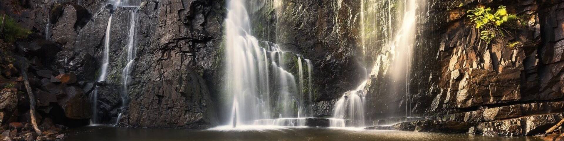 A waterfall cascading into a calm pool surrounded by rocky terrain and sparse vegetation.