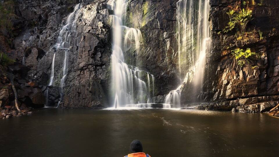 A waterfall cascading into a calm pool surrounded by rocky terrain and sparse vegetation.