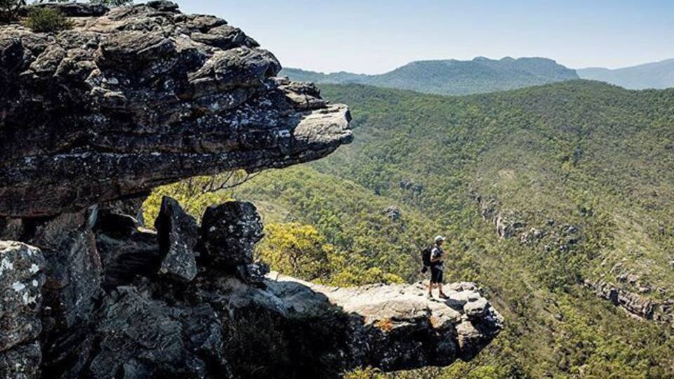 A person standing on a rock formation with a view of a forested valley and distant mountains.