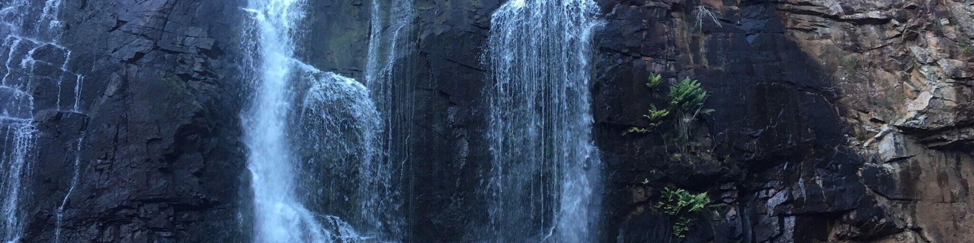Una cascada escalonada fluye sobre formaciones rocosas oscuras hacia un estanque en la parte inferior.