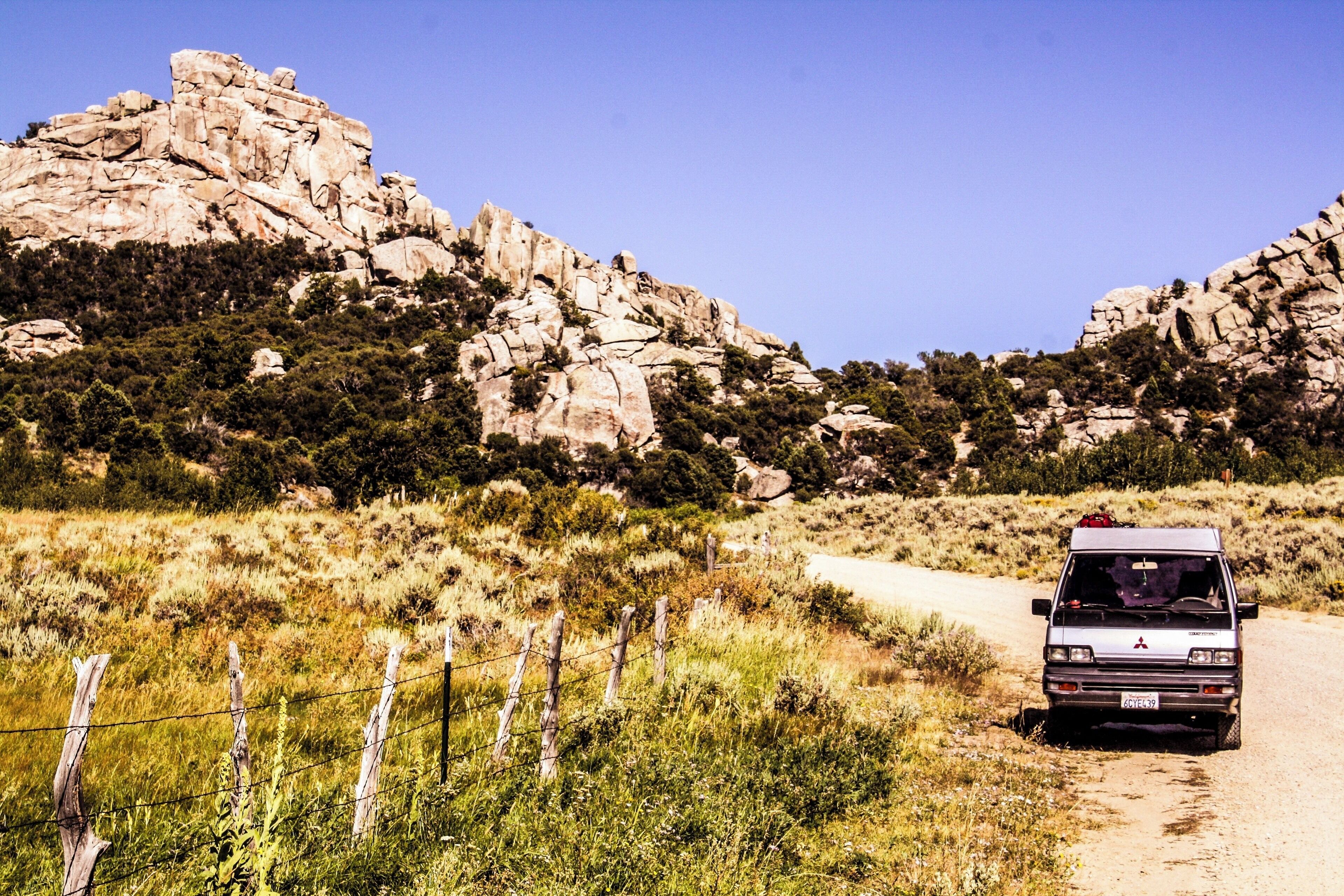 A vehicle on a dirt road with rocky mountains and sparse vegetation in the background.