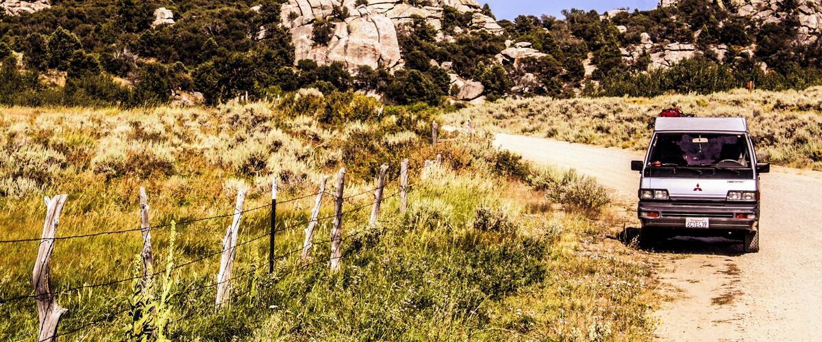 A vehicle on a dirt road with rocky mountains and sparse vegetation in the background.