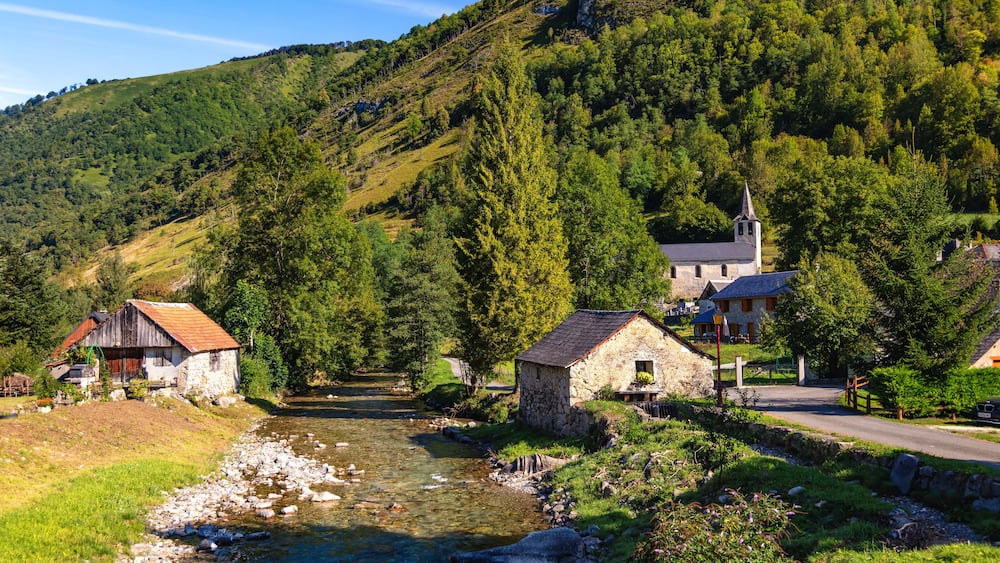 Une rivière traverse un village où se trouvent des maisons en pierre et une église située sur une colline.