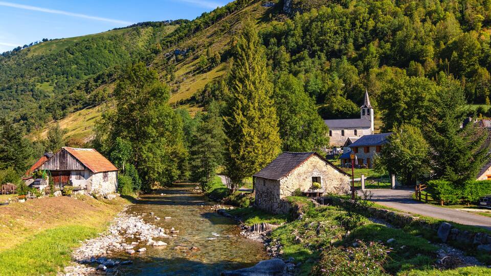 A river flowing through a village with stone houses and a church on a hillside.