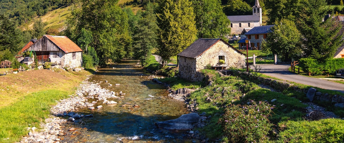 A river flowing through a village with stone houses and a church on a hillside.